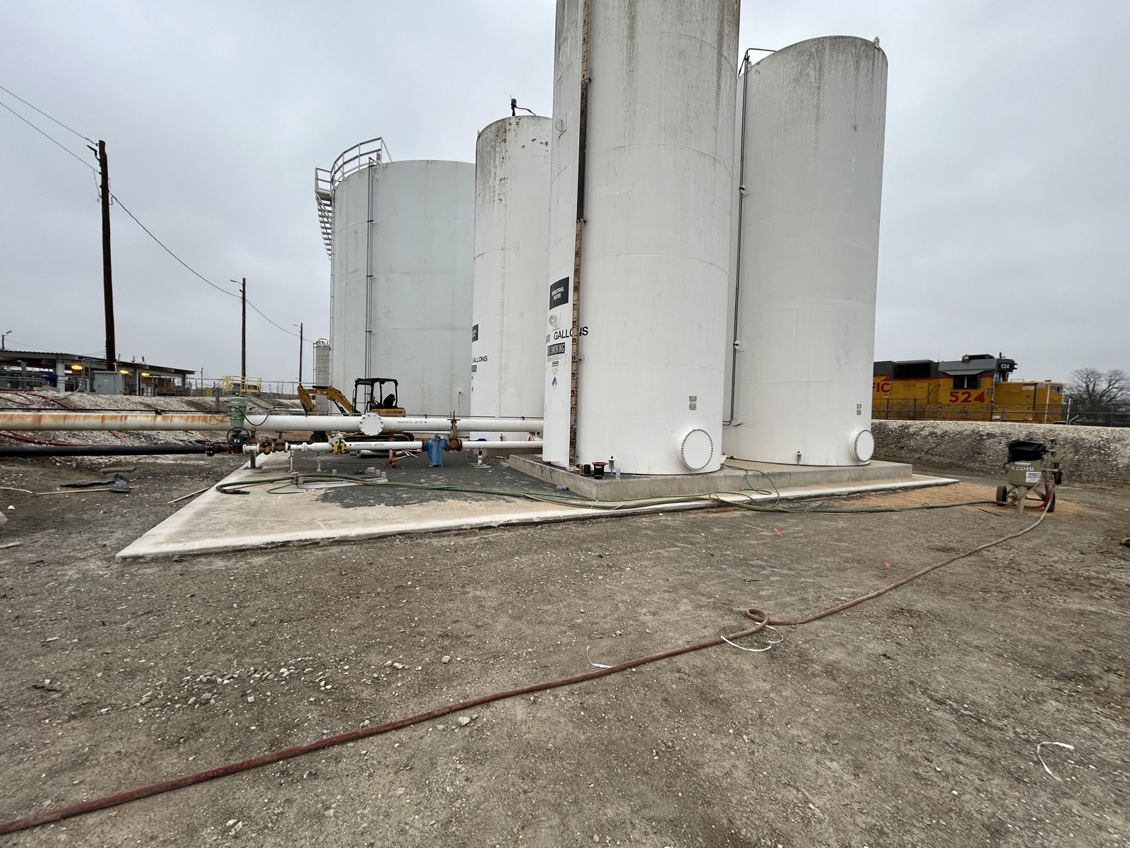 Diesel and lubricant storage tank area before liner installation, showing concrete foundations, piping, and containment berms