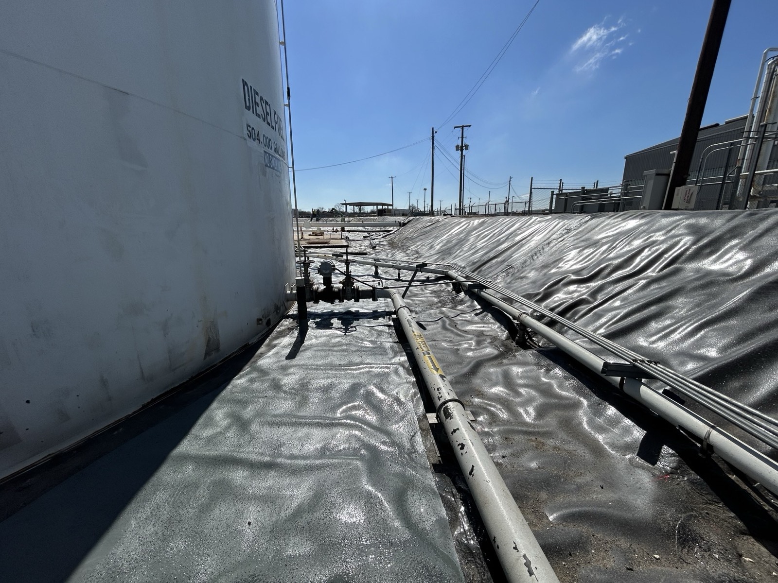 Completed liner and PHX6700 detail treatment around a diesel storage tank, piping, and sloped containment berm